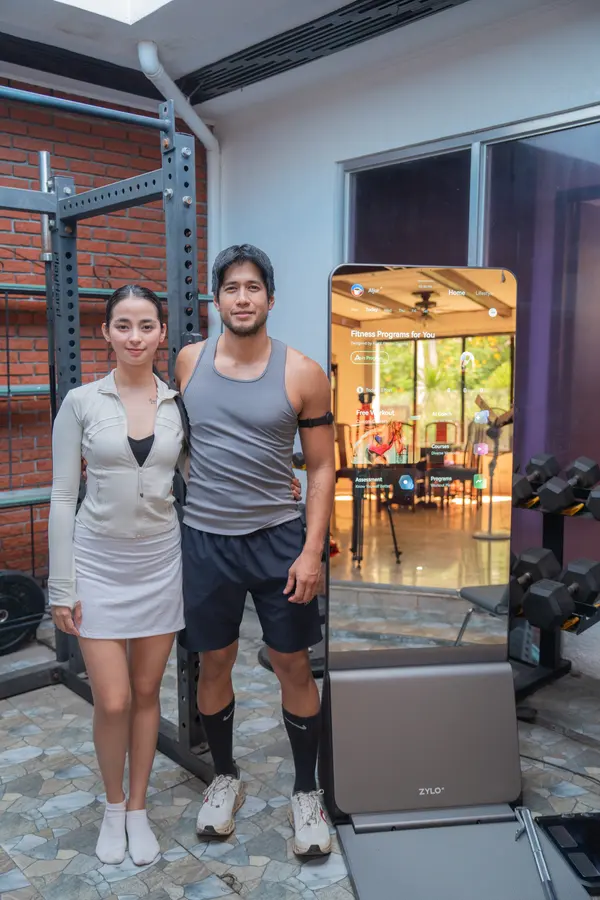 Aljur and AJ stand side by side next to a ZYLO K1 smart mirror with its screen lit.