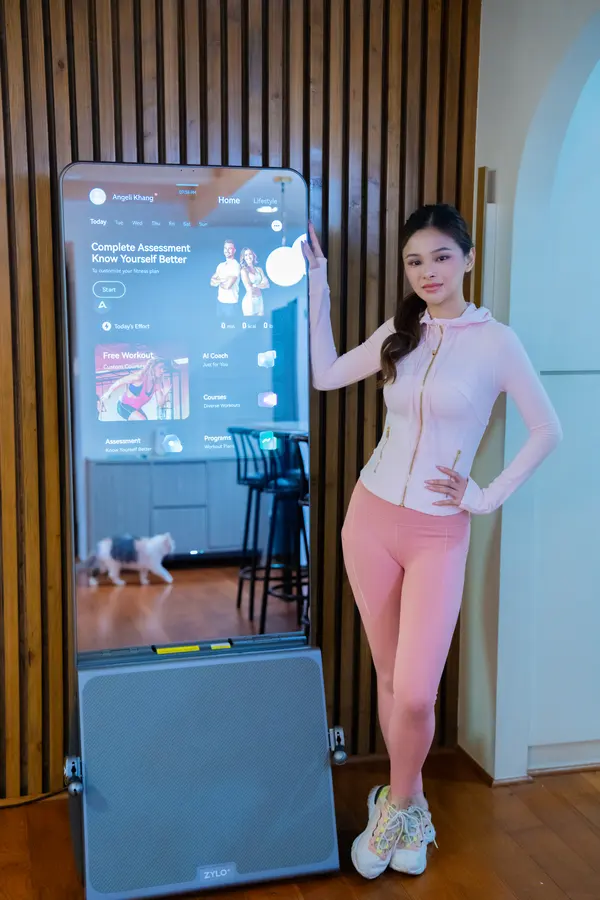 Angeli Khang poses beside a ZYLO K1 smart mirror, its screen lit with her home screen.