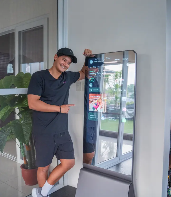 Daniel Matsunaga smiles and points at a lit ZYLO K1 screen showing his workout plan.