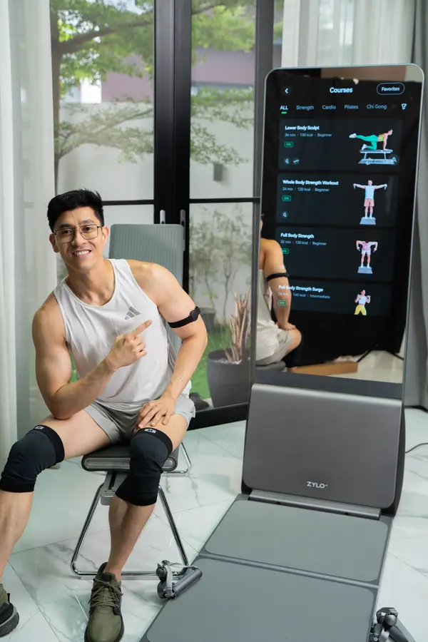 Doc Alvin smiles and points, seated beside a ZYLO K1 with its workout screen lit.