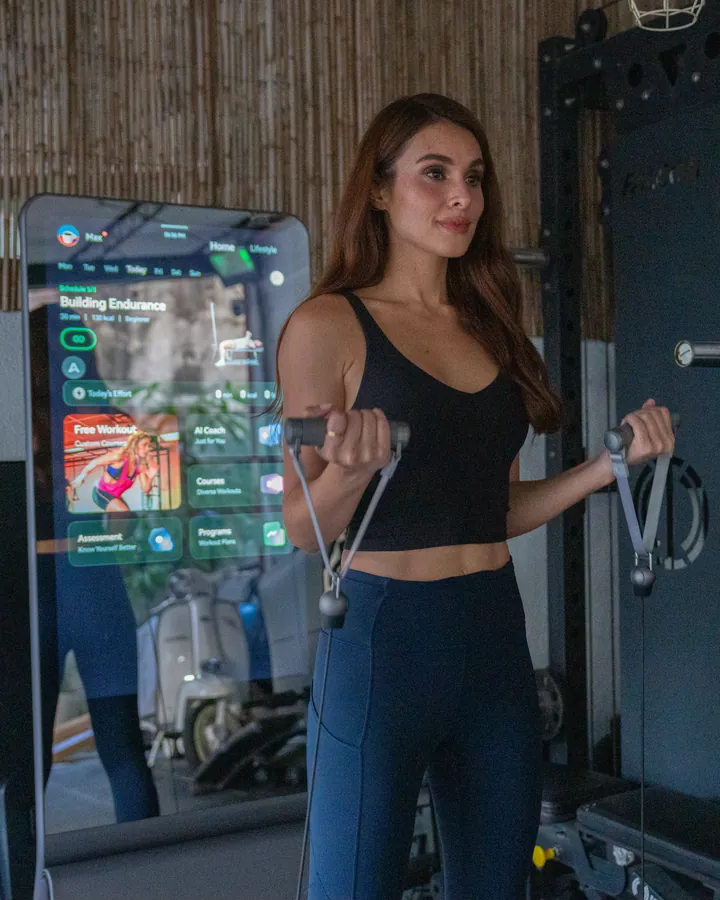 Max Collins trains with cable handles beside a lit ZYLO K1 screen showing a Building Endurance workout.